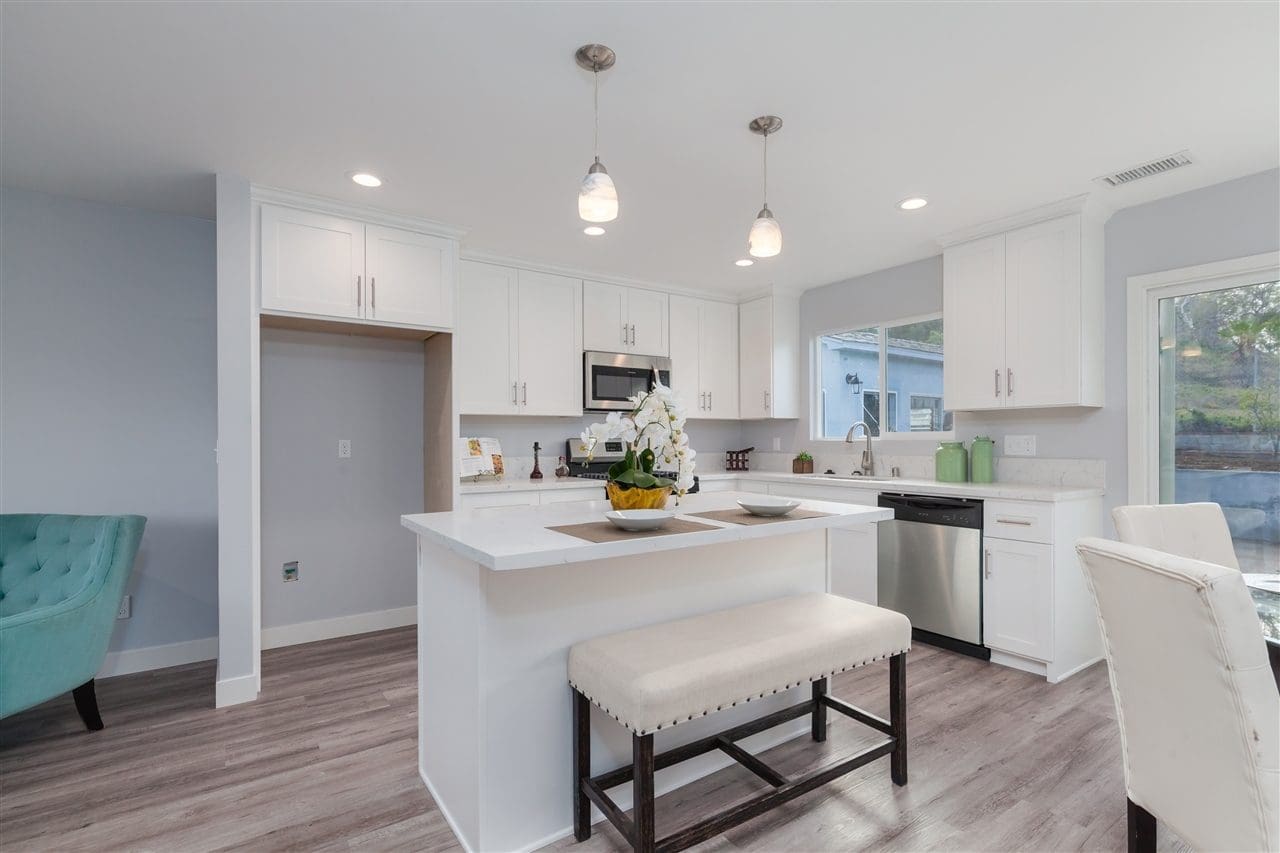 A kitchen with white cabinets and wood floors.